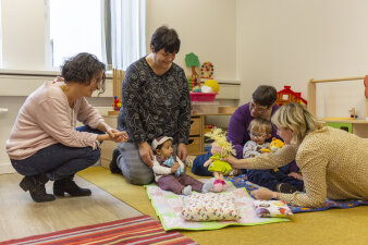 vier Frauen sitzen auf dem Boden und spielen mit zwei kleinen Kindern