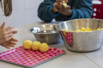 Kinder formen Thüringer Klöße und legen diese auf ein rosa Tablett mit roten Punkten.