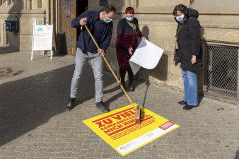 ein Mann bringt ein Plakat mit einem Besen auf dem Boden auf, zwei Frauen stehen daneben