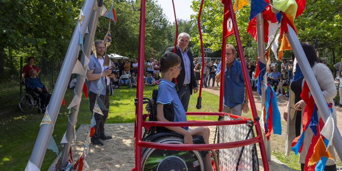 ein Kind im Rollstuhl auf einer Rollstuhlschaukel, mehrere Menschen im Hintergrund