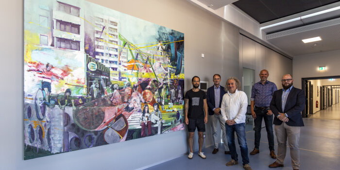 Ein modernes großformatiges Gemälde hängt an einer Wand auf einem langen Flur, daneben stehen fünf Männer.
