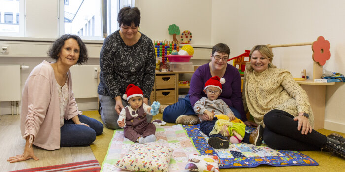 vier Frauen sitzen mit zwei Kindern auf dem Boden, die Kinder tragen Weihnachtsmannmützen