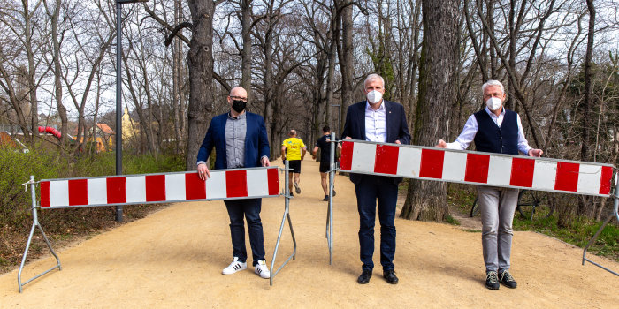 Drei Männer stehen auf einer Weg und entfernen rot-weiße Absperrgitter