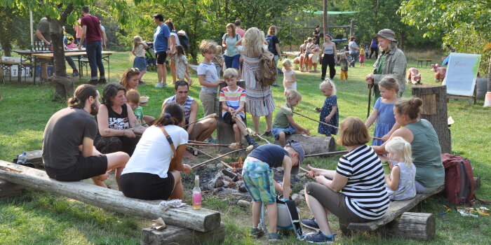 eine Gruppe von Kindern und Erwachsenen sitzt am Lagerfeuer und grillt Stockbrot
