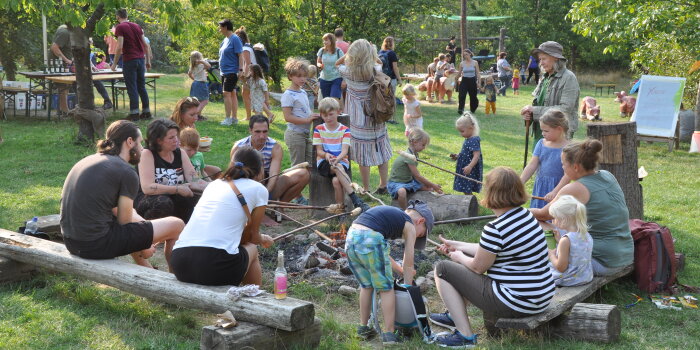 Foto: Tag der offenen Tür 2020 auf der Fuchsfarm © Stadtverwaltung Erfurt / Jens Düring eine Gruppe von Kindern und Erwachsenen sitzt am Lagerfeuer und grillt Stockbrot