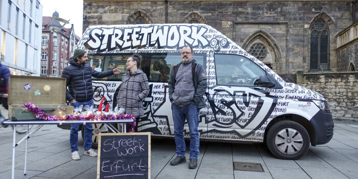 drei Personen stehen vor einem mit Graffiti gestalteten Bus, auf dem "Streetwork" steht