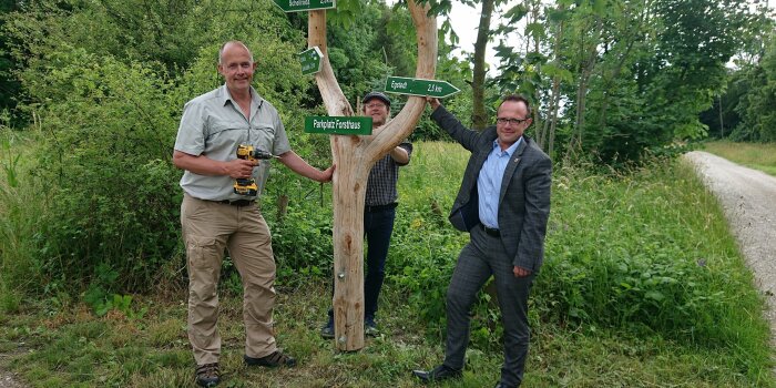 drei Männer stehen an einem Wegweiser, der verschiedene Wanderwege ausschildet