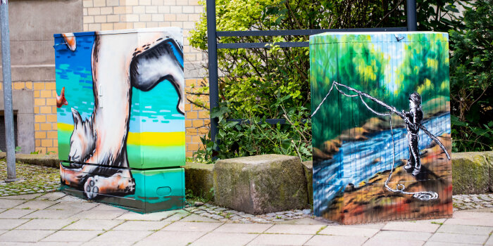 zwei mit Graffiti gestaltete Stromverteilerkästen an einer Straße