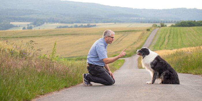 ein Mann kniet mit erhobenem Finger vor einem Hund