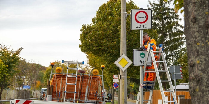 Ein Mann steht auf einer Leiter und demontiert Verkehrsschilder, die die Umweltzone ausweisen.