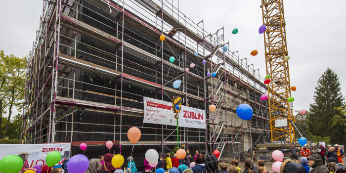 Menschen lassen Luftballons vor einem Gebäude-Rohbau steigen