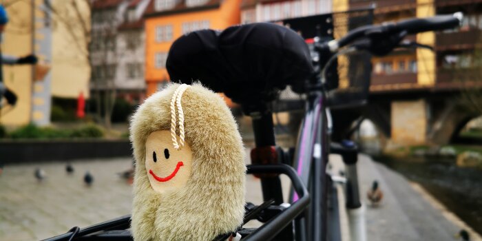 eine Plüsch-Puffbohne auf dem Gepäckträger eines Fahrrads, im Hintergrund die Erfurter Krämerbrücke