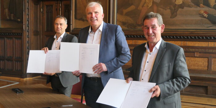 drei Männer halten eine unterschriebene Vereinbarung in der Hand und richten sie in Richtung Kamera