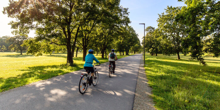 zwei Radfahrer fahren auf einem asphaltierten Weg durch einen Park