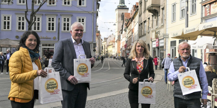 zwei Frauen und zwei Männer halten Papiertüten in der Hand, auf denen "Heimat shopper" steht