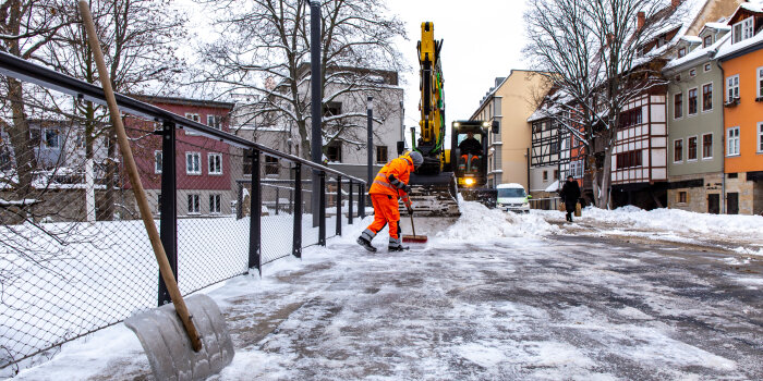 Ein Mann schiebt Schnee zusammen zur Schaufel eines Baggers.