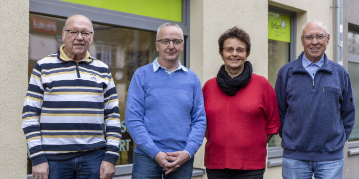 Drei Männer und eine Frau stehen in einer Reiher und schauen in die Kamera.