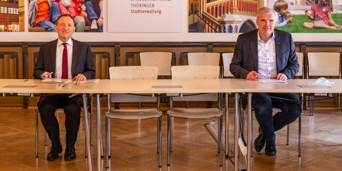zwei Männer sitzen mit Abstand an einem Tisch und unterzeichnen Verträge