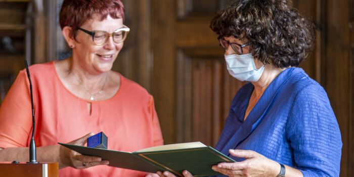 Foto: Verleihung des Ehrenbriefes an Dr. Marina Moritz © Stadtverwaltung Erfurt Zwei Frauen stehen nebeneinander. Die linke Frau übergibt der rechten eine Mappe und ein kleines Kästchen.