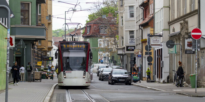 Eine Straßenbahn fährt auf einer engen Straße, rechts und links sind Häuser zu sehen.