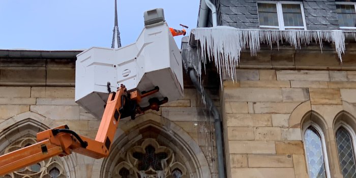 Ein Mann in einem Hubsteiger entfernt an einem Dach Eiszapfen.