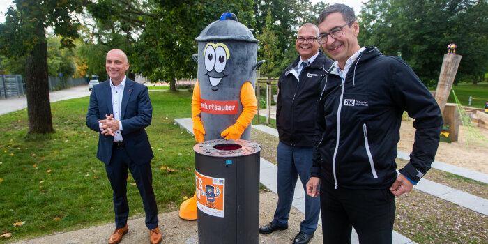 Foto: Mit Wortwitz gegen Müll © Bild13 SportPresseFotos / Christian Fischer drei Männer und ein lebensgroßes Mülltonnen-Maskottchen stehen an einem Papierkorb in einem Park