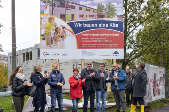 Acht Männer und Frauen stehen in einer Reihe unter einem großen Schild und klatschen.