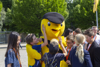 mehrere Kinder umringen eine lebensgroße Werbefigur, einen gelben Vogel