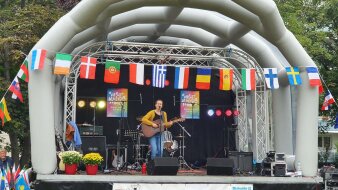 Eine Frau mit Gitarre auf einer Bühne, umrahmt von zahlreichen farbigen Länderflaggen