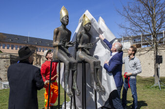 mehrere Personen ziehen eine weiße Plane von drei Skulpturen