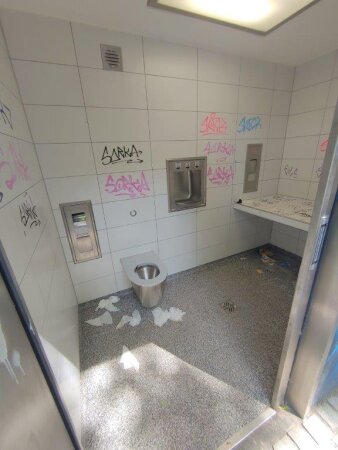 Innenraum einer öffentlichen Toilette, an den Wänden Graffiti, auf dem Boden Müll