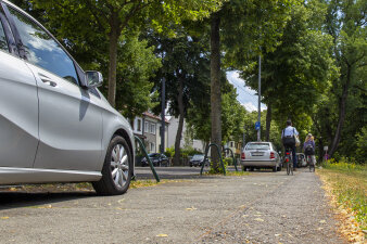 zwei Radfahrer fahren auf einem Weg, auf dem auch Autos parken