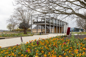 im Vordergrund ein Blumenbeet und ein breiter Weg, im Hintergrund ein modernes Gebäude