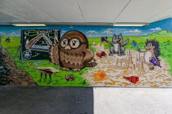 eine mit Graffiti gestaltete Wand zeigt verschiedene Motive wie Eule, Katze und Igel