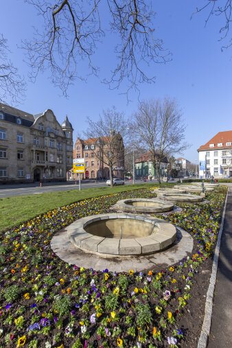 ein Blumenbeet rund mehrere steinerne Brunnenbecken 