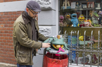 eine Person setzt einen Frosch aus Stoff auf einen Mülleimer