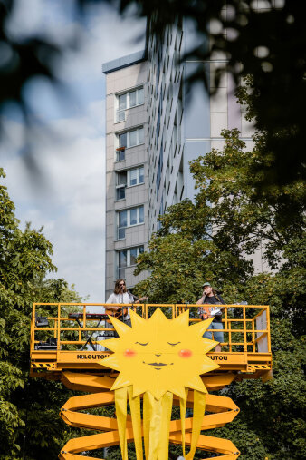 Eine orangefarbene Hebebühne, dekoriert mit einer großen Sonne, und zwei Sängern mit Gitarre darauf