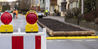 Ein frisch angelegtes Bett für Pflanzen neben einer Straße. Im Vordergrund steht eine Verkehrsbake.