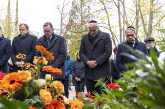 Mehrere Personen verneigen sich Blumenkränzen.