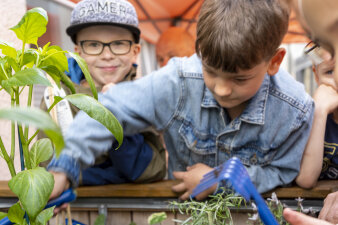 Zwei Jungen pflanzen Gemüse in ein Beet. Einer schaut freudestrahlend in die Kamera.