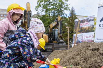 Drei Kinder spielen mit einer Schaufel im Sand.