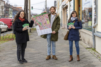 zwei Frauen und ein Mann stehen auf einem Gehweg und halten einen Stadtplan in die Kamera