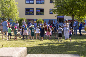 Viele Kinder tanzen zu einem Lied. Erwachsene stehen dabi und schauen zu. 