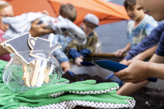 Handschuhe und Gartenwerkzeug im Vordergrund. Im Hintergund sind Kinder.