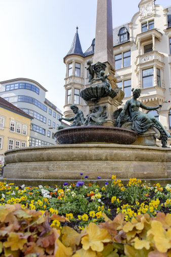 ein Blumenbeet rund um einen steinernen Brunnen mit Figuren