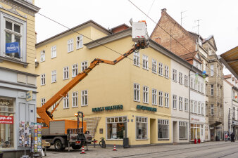 ein Hubwagen steht zwischen zwei Häusern an einer Straße, im Korb sind Arbeiter