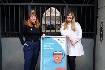 Zwei Frauen stehen an einem Aufsteller mit Plakat, auf dem "Auf einen Kaffee bei erna" steht.