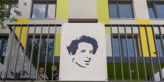 Vor einem Gebäude hängt ein großes Schild mit dem Porträt einer Frau.