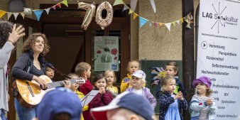 Zwei Erwachsene und viele Kinder singen gemeinsam ein Lied.