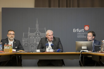 Drei Männer sitzen an einem Tisch und beantworten Fragen. 
